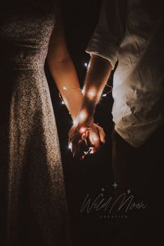 two people holding hands in the dark with lights on their fingers and one person wearing a dress