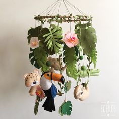 a mobile with stuffed animals and plants hanging from it's sides in front of a white wall