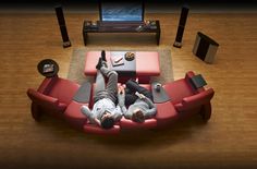 two people laying on a red couch in front of a tv