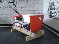 a red and white boat shaped bed sitting on top of a wooden platform in front of a brick wall