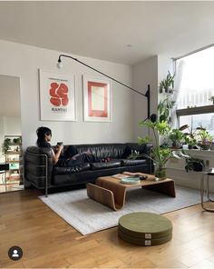 a woman sitting on a black couch in a living room next to a table and potted plants