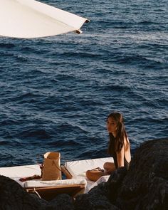 a woman sitting on the edge of a boat in the ocean next to rocks and an umbrella