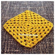 a yellow crocheted square sitting on top of a carpet