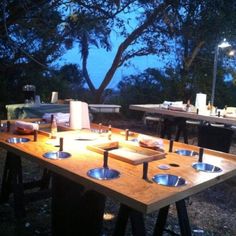 a wooden table topped with metal bowls under a tree