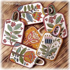 four hand painted ceramic tags with flowers and leaves on them, sitting on a wooden surface