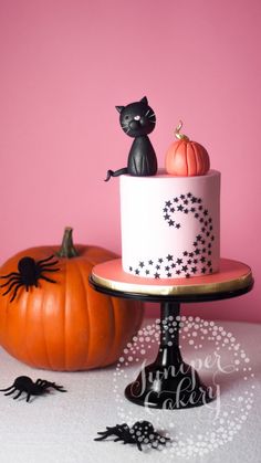 a halloween cake decorated with black cats and pumpkins on a table next to a pink wall