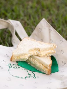 a sandwich sitting on top of a white paper bag in the middle of some grass