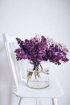 a glass jar filled with purple flowers sitting on top of a white chair