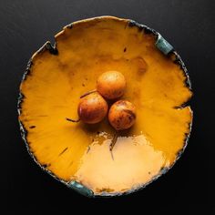 three oranges in a yellow bowl on a black surface