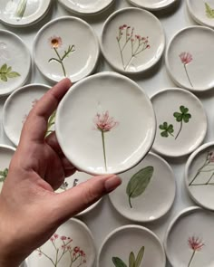 a hand holding a plate with flowers painted on it in front of many other plates