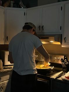 a man cooking food in a kitchen with white cabinets