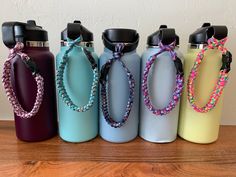 five different colored water bottles are lined up on a wooden table and one has a beaded chain around the neck