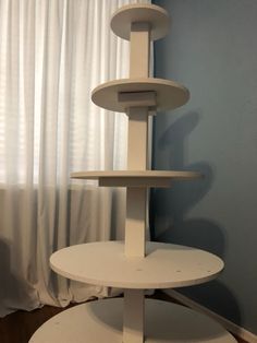 a three tiered white cake stand in front of a window with curtains behind it