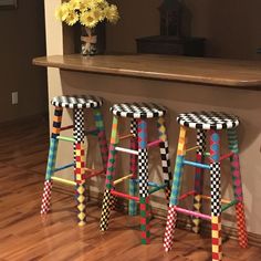 three colorful stools sitting on top of a hard wood floor next to a counter