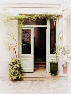 an open door to a white building with potted plants