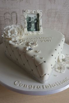 a heart shaped cake decorated with white frosting and flowers on a table next to a photo frame