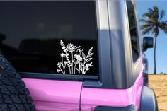 a pink jeep parked on the beach with flowers decal on it's side