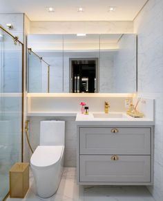 a white toilet sitting next to a bathroom sink under a mirror above a walk in shower