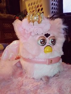 a white stuffed animal wearing a tiara on top of a pink fluffy bed covered in toys