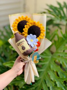 a hand holding a bouquet of sunflowers with a bottle of brown stuff in it