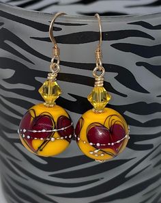 Beautiful lampwork beads in a mustard yellow with burgundy hearts.  They have sterling silver droplets on the outside.  I paired them with gorgeous yellow Swarovski crystals.   They are securely wire wrapped and have bright gold daisy spacers between them.  I suspended them from 14k gold filled ear wires.     Earrings measure 1.5" long Will come gift packed. Follow me on Facebook and Instagram and NYC Fashion Connection for exclusive coupon codes and sneak previews! Yellow Heart-shaped Jewelry For Valentine's Day, Red Heart-shaped Hand Painted Jewelry, Yellow Heart Beads Jewelry For Valentine's Day, Yellow Jewelry With Heart Beads For Valentine's Day, Valentine's Day Yellow Jewelry With Heart Beads, Yellow Heart Beads Jewelry For Gift, Yellow Heart-shaped Jewelry, Yellow Czech Glass Round Bead Earrings, Yellow Czech Glass Earrings For Gifts