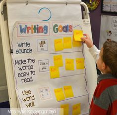 a young boy writing on a bulletin board with post - it notes attached to it