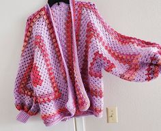 a pink crocheted sweater hanging on a hook next to a white wall with a black hanger