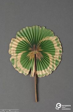 a green and white paper fan sitting on top of a gray wall next to a wooden stick