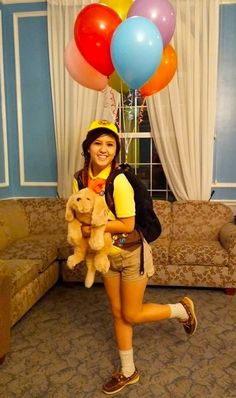 a woman holding a teddy bear in her hands and balloons around her head while smiling at the camera