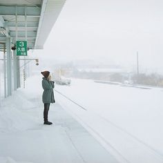 a woman standing on the side of a snow covered train platform while talking on her cell phone