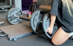 a woman squatting down next to a bench with two dumbbells on it