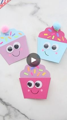 three paper cupcakes with faces and sprinkles on them