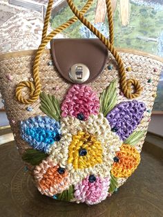 Adorable vintage straw purse adorned with a giant colorful flower and leaves stitched on. Stiff polypropylene rope handle stays upright. Zippered compartment in shiny "patent leather" off white interior. Faux leather covers the top between the handles and is held on by a twist clasp. 11" wide at top 10" high 4" deep at base Boho Mcm, Woven Purse, Straw Purse, Flower And Leaves, Boho Purses, Bags Aesthetic, Embroidered Bag, Rope Handles, White Interior