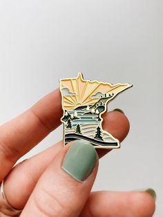 a person holding a pin with a lake and mountains on it in their left hand