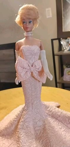 a barbie doll wearing a pink dress and white gloves on top of a wooden table