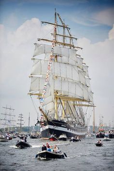 a large white sail boat in the water with other boats around it and people on small boats