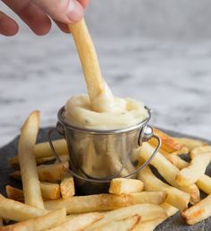 a person dipping something into a small metal container filled with french fries on top of a stone slab