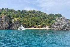 there is a boat that is in the water near some rocks and trees on the shore