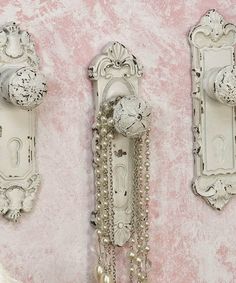 two ornate white wall mounted clocks with chains and pearls hanging on the wall next to each other