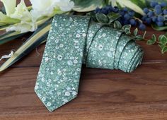 a green floral tie sitting on top of a wooden table next to flowers and greenery