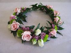 a floral wreath with pink roses and green leaves on a white tableclothed surface