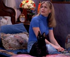 a woman sitting on top of a bed with a black cat in front of her