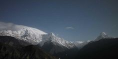 the mountains are covered with snow and stars in the night sky, as seen from below