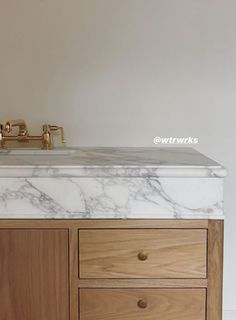 a bathroom vanity with marble counter top and wooden cabinet drawers, gold faucet