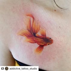 a goldfish tattoo on the back of a woman's shoulder is shown in this image