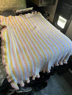 a crocheted blanket on top of a bed in a room with black shoes