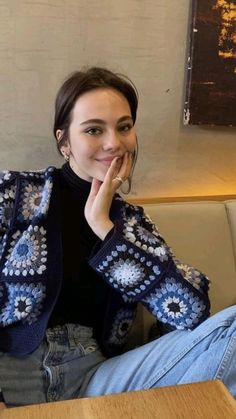 a woman sitting at a table with her hand on her face and looking into the camera