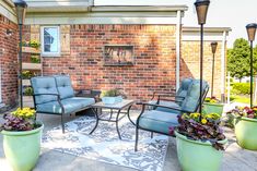 a patio with chairs, table and potted plants on the ground next to a brick building