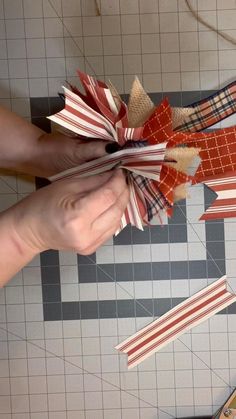 two hands are holding red, white and orange ribbons on a tiled floor with scissors