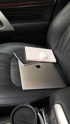 an apple laptop sitting on top of a black leather seat in a car or truck